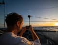 "Guyot"-Skipper Benjamin Dutreux macht ein Foto vom Sonnenuntergang. Da ahnt er noch nichts von dem Problem, das sein Team später zur Aufgabe der dritten Etappe zwingt