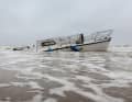 Le bateau de 6,50 mètres de long est à moitié hors de l'eau, à moitié sous l'eau et le sable sur la plage.