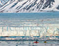 Due dei partecipanti al viaggio remano in kayak fino al bordo di un enorme ghiacciaio