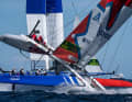 Il team canadese SailGP con il timoniere Phil Robertson sfiora il capovolgimento. Sullo sfondo, il team francese con il timoniere Quentin Delapierre