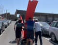 Bei einem gemeinsamen Besuch halfen Albert Schweizer (r.), Tim Kröger und weitere Teammitglieder Boris Herrmann in Lorient mit einem Foil-Transport durch den Hafen La Base.