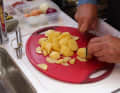 To slice the potatoes, first cut them in half lengthways and then cut them into thin slices. This prevents them from rolling away