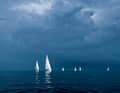 The sails of the yachts shine bright white against a dark grey wall of clouds. What's coming towards them?