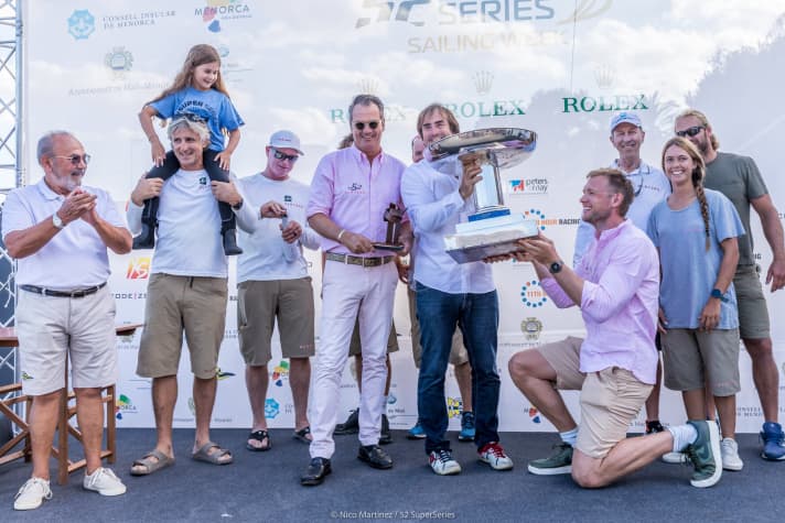   Die glücklichen Sieger von Menorca: Harm Müller-Spreer in der Mitte im rosa Hemd mit Teilen seiner Crew und einem kleinen Fan sowie dem begehrten Royal Cup
