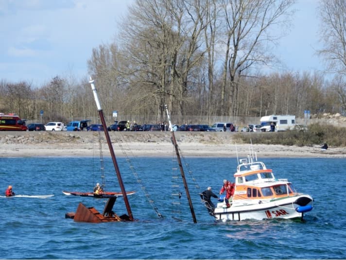   Der 78-jährige Mitsegler klammert sich bis zum Eintreffen der Seenotretter an die Wanten. Aufmerksame Kajakfahrer bleiben in seiner Nähe. Am Ufer steht der Rettungsdienst bereit