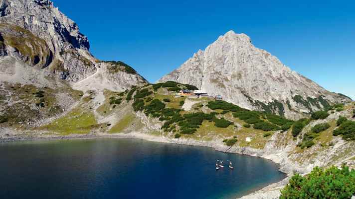 Im Morgenlicht thront die Sonnenspitze über dem Drachensee. Die Wanderer in der Coburger Hütte ­schlummern noch. ­Lange genießt das Team die grandiose ­Aussicht nicht – es ­warten noch acht Seen auf sie.
