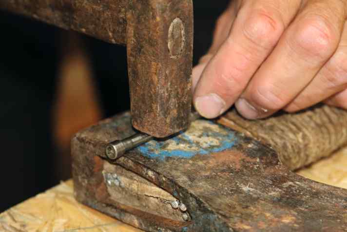 Um die Metallbolzen später wieder einbauen zu können, richtet Oli diese zuerst. Setze die Schrauben in die Bolzen ein, lege diese auf eine harte Unterlage und klopfe sie mit vorsichtigen Hammerschlägen wieder gerade.