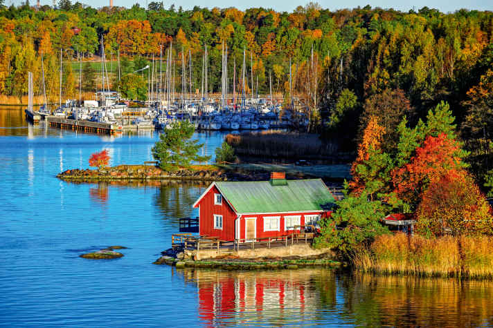 Cabina estiva rossa o mokki in una foresta dai colori autunnali sulla riva rocciosa del Mar Baltico. Isola di Ruissalo, arcipelago di Turku, Finlandia