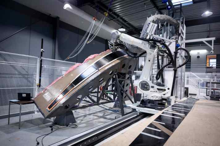   Il team sta aprendo nuove strade nella costruzione dei foil: per la prima volta nella classe Imoca, un robot posiziona i tappetini di carbonio con una precisione di un centesimo di millimetro.