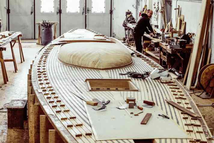 Das Deck entsteht, während der Rumpf gebaut wird, gleichzeitig daneben. Den Bootsbauern ist es damit möglich, jederzeit direkt Maße abzugleichen. Die Decksbalken werden dafür in modellprovisorische Balkweger eingelassen. Auf dem darauf verlegten Sperrholzdeck entsteht ein Stabdeck aus Oregon Pine. Der in allen Ebenen runde Aufbau kostet die Bootsbauer viele Stunden Arbeit