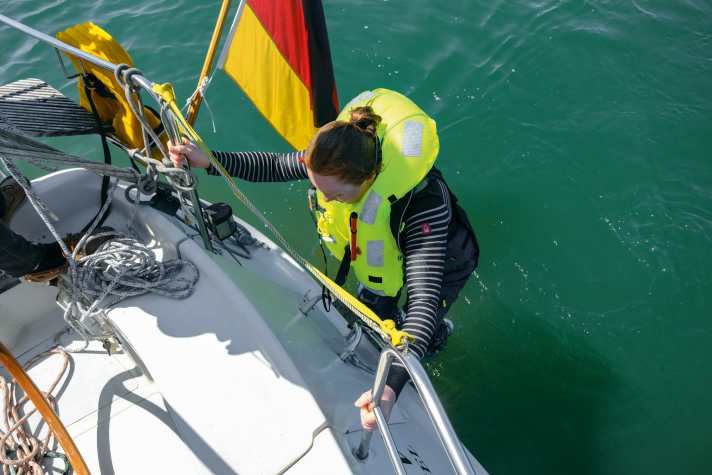 If the crew member is still able to climb on deck under their own power, the bathing ladder is the easiest option. Use the line to guide the casualty to the stern. In heavy seas, however, a pitching stern can be dangerous