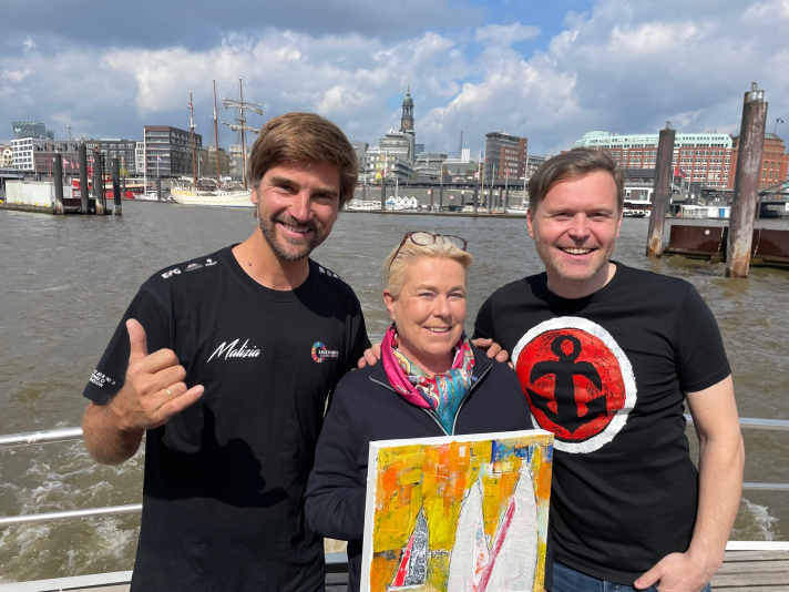   Bei einer Frühlingsbarkassenfahrt mit Freunden auf der Elbe: Hubert Neubacher (Barkassen-Meyer), Künstlerin Heinke Böhnert und Boris Herrmann. Zur Elb-Ausfahrt hatte der "Erfinder der Kunst-Barkassen" und Herrmann-Fan Neubacher geladen. Dafür gab es von Heinke Böhnert in Erinnerung an die spannende Vendée-Globe-Zeit und als Vorgeschmack auf noch kommende Gipfelstürme ein Bild als Dankeschön