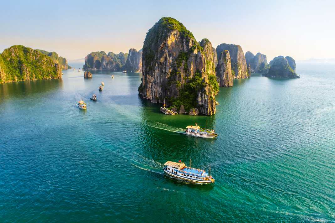Ausflugsboote in langer Prozession auf der Halong-Bucht im Norden Vietnams nahe der Grenze zu China. Monumentale Karstfelsen prägen die Landschaft