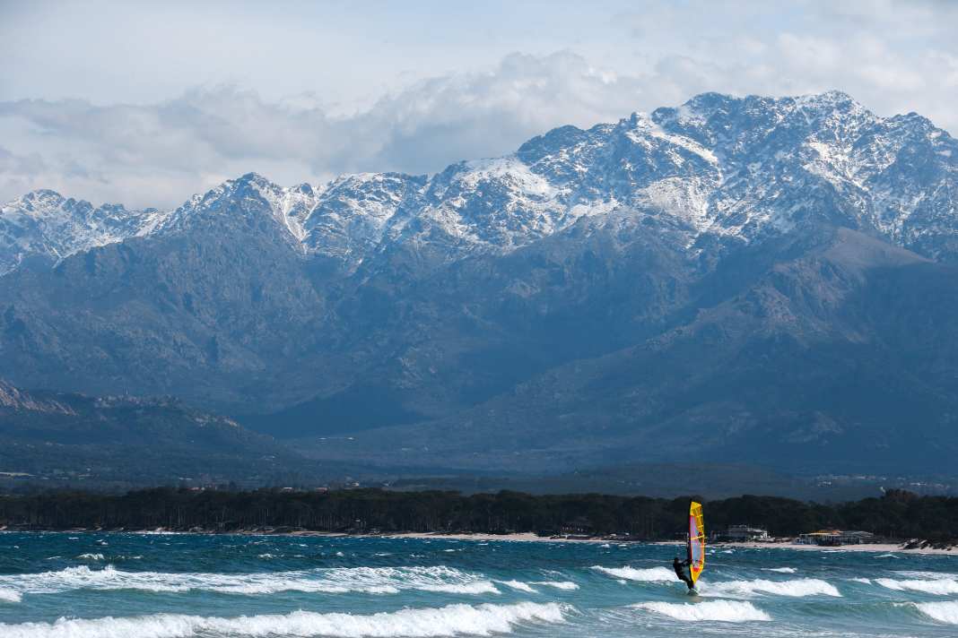 In der Bucht von Calvi surft man mit Blick auf die imposante Kulisse Korsikas. Die Berge rund um den über 2700 Meter hohen Monte Cinto sind im Frühjahr oft noch vom Schnee bedeckt.