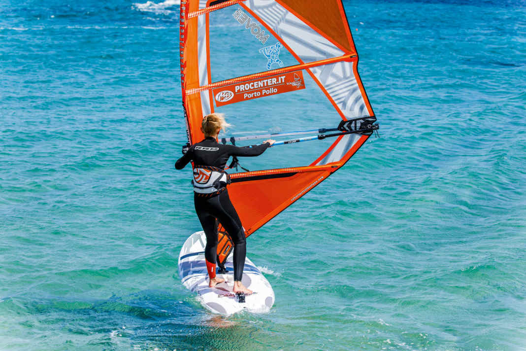 Die Halse beim Windsurfen Schritt für Schritt: Hole wie immer nach dem Start erstmal etwas Schwung und bereite die Halse vor, indem du die Segelhand am Gabelbaum etwas nach hinten in Richtung Gabelbaumende verschiebst.