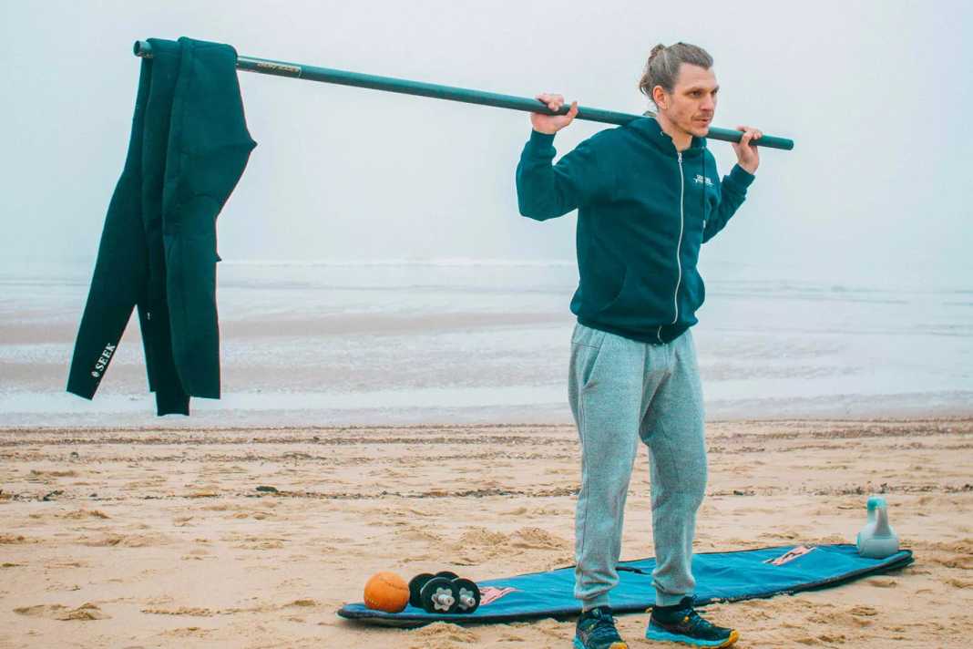 No exercise trains more muscles in the body. The squat is still the most perfect exercise of all and should not be missing here either. But here I have a modified form for you. Take your pole and hang a weight on one end. I have used my Neo. You stand at the other end of the pole. Even if a wetsuit doesn't seem heavy at first, the leverage forces should not be underestimated and can still put a lot of strain on you, as you now have to keep your balance and your entire core muscles have a lot to do.
