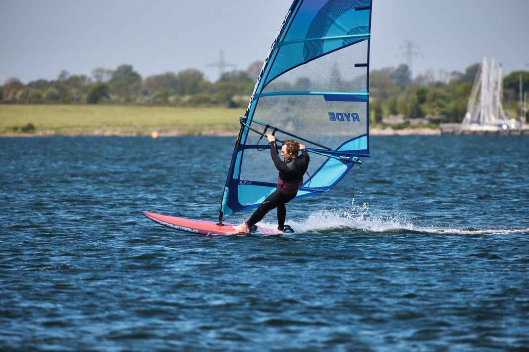 1st preparation phase: Before you think about taking the step into the straps, you first need to get up to the necessary speed. To do this successfully, you should set your board up on a light space wind course, i.e. the course diagonally away from the wind. The space wind course is the fastest course in surfing and therefore the chance of making it over the glide threshold is highest here. Hook into the harness, turn your upper body forwards - as described on the previous page - and make sure that your front foot is turned in the direction of travel on the deck. By turning the body forwards (front foot, chest), the power transfer to the board is directed forwards. If, on the other hand, the front foot is on the board at right angles to the direction of travel, the upper body automatically turns with it - this results in lateral forces that push the tail away to leeward and turn the bow into the wind. In this preparation phase, try to make contact with the strap with the front heel. This will allow you to place your foot in the strap without eye contact during the next step.
