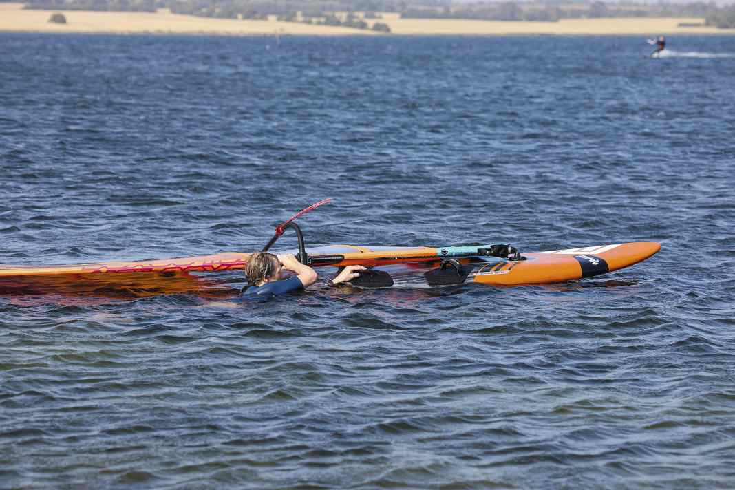 Liegt das Material richtig für den Wasserstart, muss das Segel über den Kopf gezogen werden. Dazu mit der vorderen Hand direkt über der  Gabel am Mast oder vorne am Gabelbaum zu greifen.