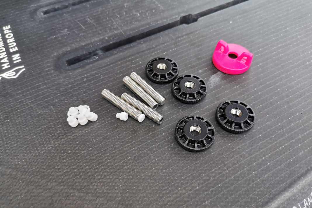 Das FoilFix Set besteht aus Stehbolzen, kleinen Spacern (weiß) zum Anpassen der Schraubenlänge, den Muttern (schwarz) und einem kleinen Werkzeug (pink)