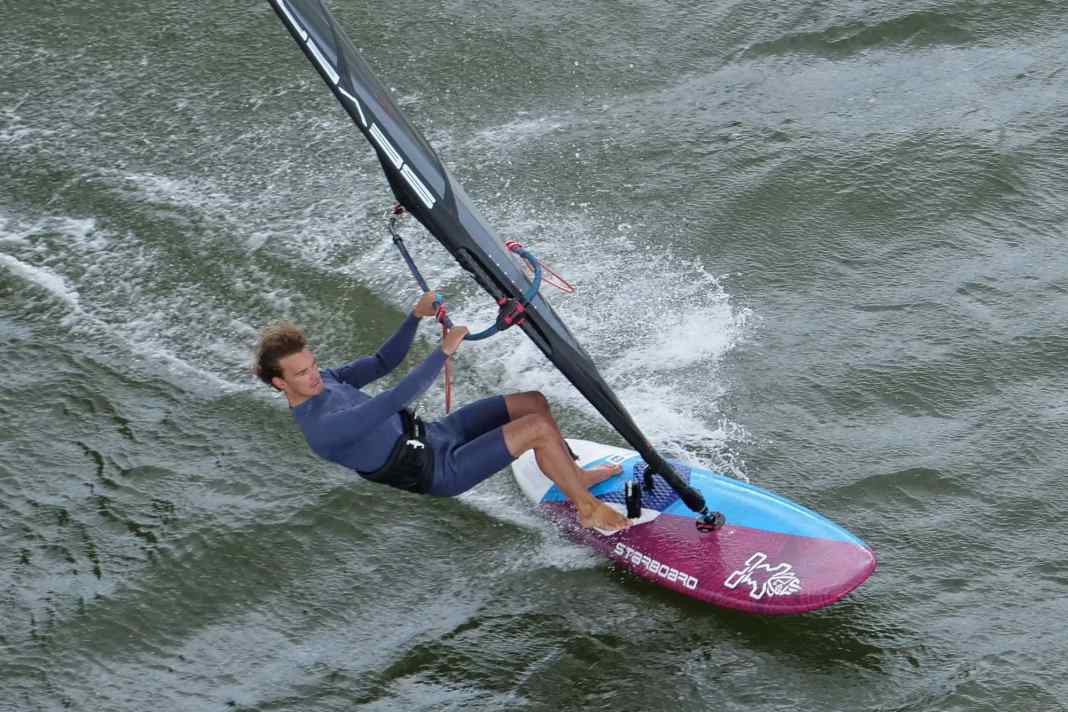 At full planing speed on a half-wind course, first take your back foot out of the loop and grip the boom as far forward as possible with your front hand.