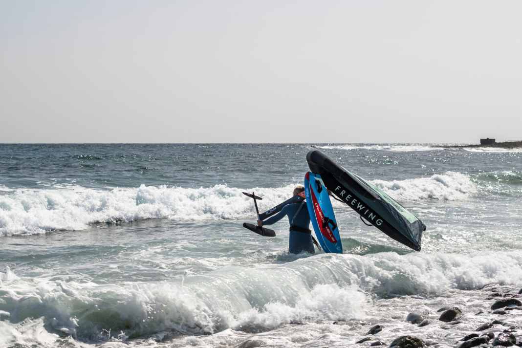 Laufe mit dem Board auf der Schulter erst vorsichtig ins Tiefe Wasser weiter