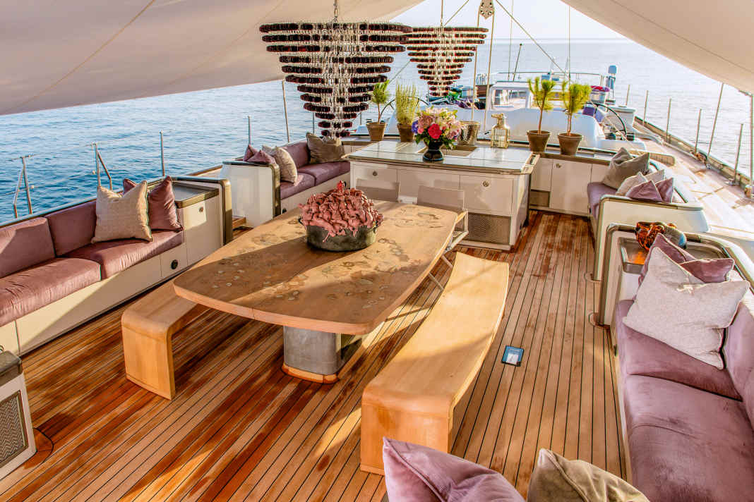 Under the awning: In the front, the large guest cockpit with dining table, two Murano candelabras hang from the main boom. It is directly connected to the galley below.  The bronze sculpture in the centre of the table is by Cuban artist Roberto Fabelo