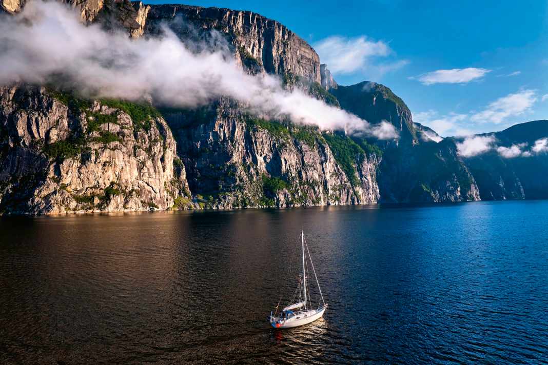 Ein schmales Wolkenband zieht entlang der Flanke einer steinernen Wand am Lysefjord. Davor die Yacht des Autors. Sie lässt die gewaltigen Dimensionen der Felsen erahnen