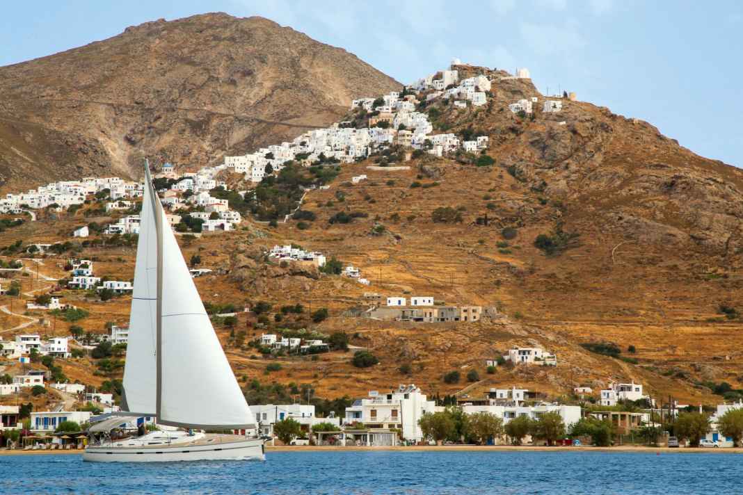 Eine Yacht segelt in der Bucht Livadi am Fuß der Altstadt von Serifos. Die thront hoch oben am Berg und ist unbedingt einen Besuch wert