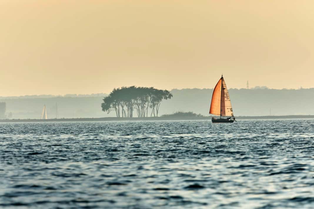 A sailing boat sets course for the Schlei in the reddish shimmering light of the evening sun.