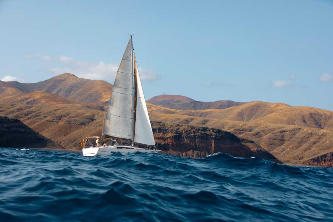 Sailing in the Atlantic swell against an impressive volcanic backdrop in the south-east of the Canary Island of Lanzarote at Playa La Casa