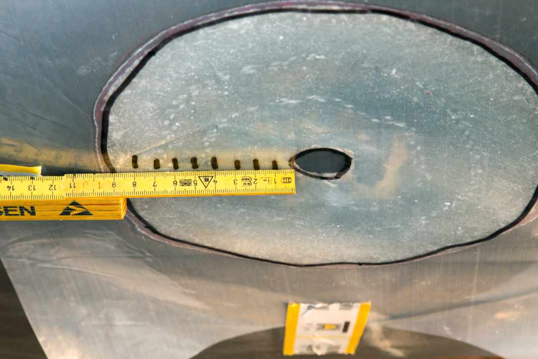 Levigare il supporto: Carteggiare intorno al foro un supporto di spessore dodici volte superiore a quello del laminato, in questo caso circa dieci centimetri. Trasferire la sagoma su un foglio di alluminio e segnare su di esso le dimensioni delle toppe in vetroresina.