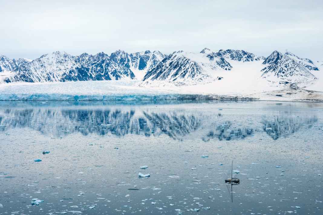 Die 66-Fuß-Aluyacht „Qilak“ im Eisfeld vor den schneebedeckten  Ber­gen und einem der Gletscher an der Westküste Spitzbergens