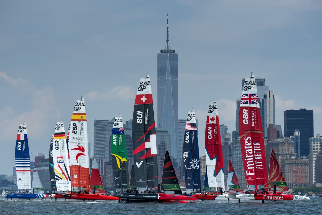 Die Flotte unter Führung des Emirates Great Britain SailGP Teams vor dem Canada SailGP Team und dem USA SailGP Team passiert am zweiten Renntag des Mubadala New York Sail Grand Prix in New York, USA, das One World Trade Center und die Skyline von New York City