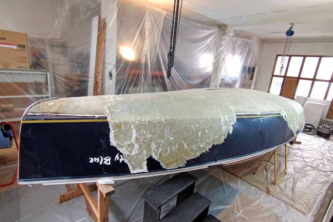 In a fortunately available workshop, Maximilian Kolb strips the laminate layers, which are barely separating from each other, from the hull with a spatula