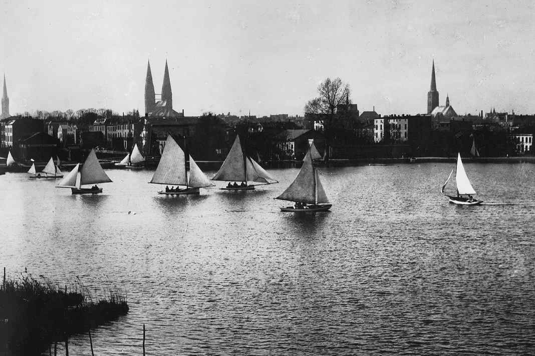 Les navigateurs du Lübecker Yacht-Club avec leurs bateaux sur la Wakenitz, avec les clochers de Lübeck en arrière-plan.