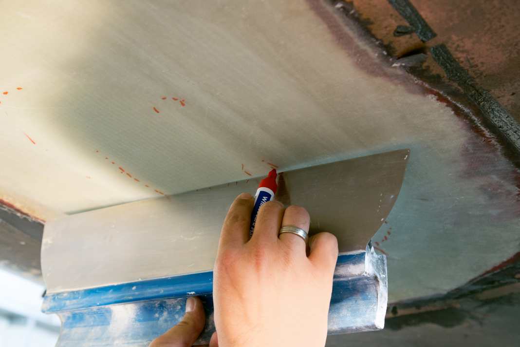 After curing, the peel ply is removed. The levelling of the laminate can then begin. Firstly, mark the raised areas that protrude beyond the hull strake. A large palette knife or a batten is suitable for this purpose