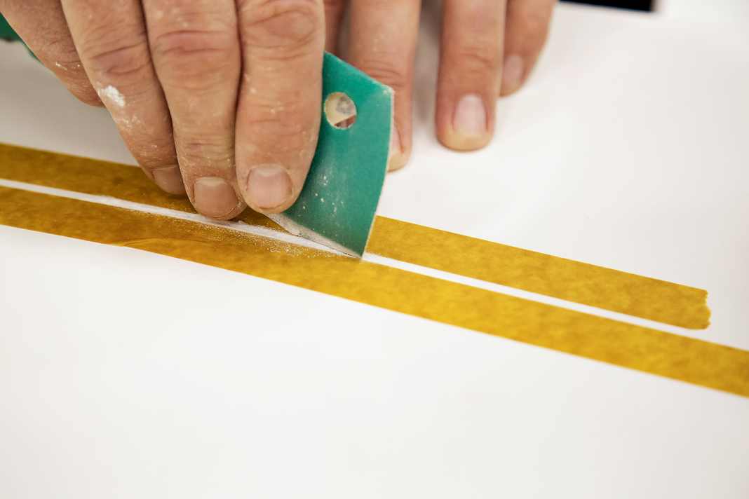 Sand the edges of the scratch at an angle with 120-grit paper. The adhesive tape protects the surrounding area from scratches