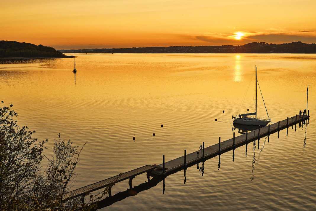 Goldener Moment. Einsam liegt eine Yacht am Steg in der Andkær Vik am Südufer des Vejle-Fjords. Lediglich ein weiteres Boot hat an einer der Muringbojen festgemacht