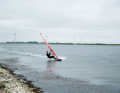 Place your back foot in front of the foot strap, unhook yourself from the harness at full planing speed and start on a light upwind to half-wind course (with your arms already bent) by gently placing only your front leg on the surface of the water first. Hold the sail close to your body, especially with your front hand. You can repeat this several times as a preliminary exercise to familiarise yourself with the feeling.