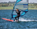 2. Der Schritt in die Schlaufe: Viele, die das Schlaufensurfen lernen wollen, wechseln zu früh in die Strap und würgen das Angleiten damit ab. Daher gilt: Erst wenn du eine stabile Gleitfahrt erreicht hast, setzt du den vorderen Fuß in die Schlaufe. Häufiges Problem: In dem Moment, wo der vordere Fuß angehoben wird, liegt es nahe, das komplette Körpergewicht auf den hinteren Fuß zu verlagern. Dieses Problem umgehst du über die richtige Trapeztechnik und eine spezielle Körperhaltung. Mit hoher Gabel und längeren Tampen kannst du Gewicht über das Trapez und die Gabel auf den Mastfuß bringen. Hänge dein Körpergewicht in dieser Phase bewusst ins Trapez und neige den Oberkörper leicht nach vorne, so als wolltest du am Mast vorbei auf die Leeseite blicken. Dein Körpergewicht lastet nun im Prinzip auf „drei Beinen“ – Mast, vorderer Fuß &amp; hinterer Fuß. In der Folge kannst du nun das „mittlere“ (= dein vorderes Bein) anheben und den Fuß in die Schlaufe setzen, ohne dass du das Heck übermäßig stark belasten musst.