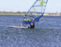 Foot on deck: If you feel enough pull, you can now put your back foot on the board. In order to keep the board on a light headwind course and not inadvertently turn back into the wind, it helps to position your foot on deck, initially turned inwards (with your toes pointing in the direction of travel). This puts your body in a forward position and, to exaggerate somewhat, your gaze goes past the front of the mast to leeward. The arms remain fully extended.