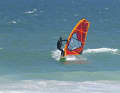 On your way towards the shore, look for a swell wave that is building up and adapt to its speed. Drop slightly on the wave face to reduce the pull in the sail and make the following side change easier. Put your front foot in front of the base plate and release your back hand from the boom to grab the new boom side.
