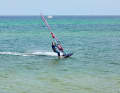 Unhook yourself from the harness in full glide and place your back foot out of the loop onto the windward edge of the board. Place your front foot out of the loop directly next to the foot of the mast.