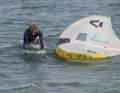 In preparation, Wesley first grabs the wing's handleash and pulls it very close to the board. He then grips the board by the edges and presses it under his body. As always, the wing lies on the downwind side of the board (leeward)