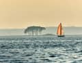 A sailing boat sets course for the Schlei in the reddish shimmering light of the evening sun.
