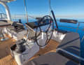 Steering position with various technical equipment: large plotter, switches for bow and stern thruster and the electric winches as well as the throttle. In front of this is a sofa facing the direction of travel.