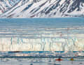 Two of the trip participants paddle to the edge of a huge glacier in kayaks