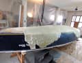 In a fortunately available workshop, Maximilian Kolb strips the laminate layers, which are barely separating from each other, from the hull with a spatula