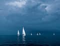 Les voiles des yachts brillent d'un blanc éclatant devant un mur de nuages gris foncé. Qu'est-ce qui se profile à l'horizon ?