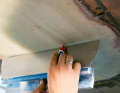 After curing, the peel ply is removed. The levelling of the laminate can then begin. Firstly, mark the raised areas that protrude beyond the hull strake. A large palette knife or a batten is suitable for this purpose